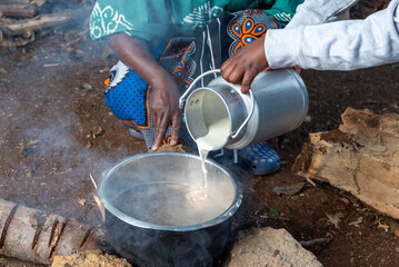 Young African teenager pouring fresh milk into pot 