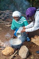 Young African teenager pouring fresh milk into pot 