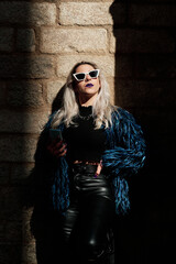 Alternative woman in sunglasses looking at sun while holding a mobile phone outdoors.