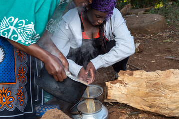 African Teenage girl helping to sieve tea into a pot