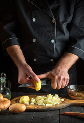 Professional chef cuts raw potatoes into pieces with a knife before preparing breakfast or dinner. Close-up of a cook hands while working in kitchen