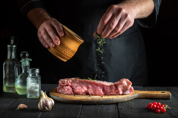 Professional chef prepares raw veal meat. Before baking, the chef adds a dry herbal seasoning to the beef. National dish is being prepared in the kitchen.