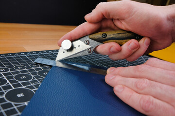 Close up hands tanner cuts special cutting knife leather piece in workshop. Craft production.