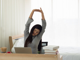 Asian young woman feeling sleepy after a long working day, working at home.  Pretty student stretching lazily after long online learning.