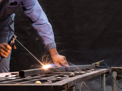 Close up, worker without any gloves welding iron pipe wih bright spark on the steel table top