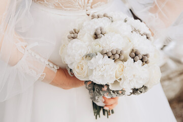 The wedding bouquet of bride in the hands on the bacground of white dress