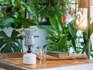 Vintage coffee pot with glass on the table along with book in the greenhouse.