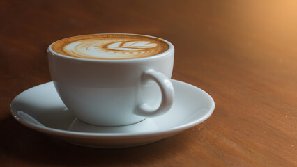 Hot coffee with latte art in white cup with saucers on wooden table