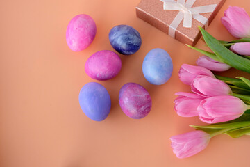 Set for Easter holiday concept. Eggs are beautifully painted in pink and purple, blue, blue color, a gift box with a ribbon and flowers tulips on a pink background