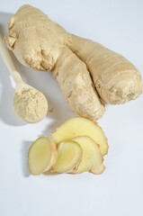 Ginger root with chopped wedges and dry powder on white plate with hard light