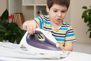 A boy of 4 years learns to hold an iron, iron clothes on an ironing board. Helper, help children to...