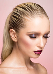 Fototapeta premium Closeup beauty portrait of young woman with makeup, hair straightened and caught in the back, isolated pink background.