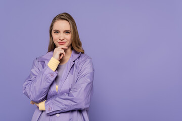 pleased young woman in trench coat isolated on purple.