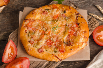 Pizza with cheese and tomatoes on a wooden background close-up