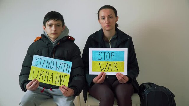 Refugee woman and boy holding motivational packards with text Stop war and Stand with Ukraine against armored conflict. Crisis, peace, stop aggression in whole world