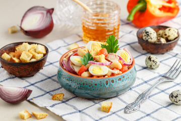 Delicious salad of chicken fillet, bell pepper, white beans, quail eggs, bread croutons, red onion and parsley with a sauce of olive oil, mustard and honey. Selective focus