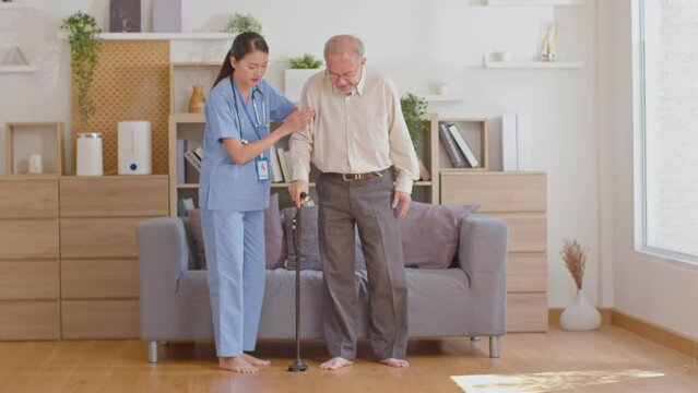 Beautiful doctor helping old man at clinic. Holding a senior patient with walking stick. Elder man using walking cane at nursing home with hand support his back. Prevent accident at nursing home.