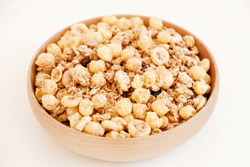 Dry muesli with cornflakes, nuts and raisins in a wooden bowl on a white background
