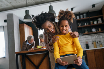 Happy african american mother helps teenage daughter with homework using digital tablet