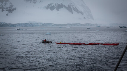 Ein Schlauchboot zieht eine Reihe von roten Kanus durch eine Bucht samt Gletscher und Eisbergen in...
