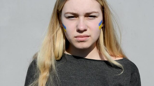 Portrait of Ukrainian teen blond hair girl with flag of Ukraine on cheek,patriotic symbol. Pray for Ukraine,war 2022 