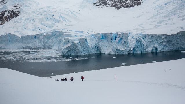 Eine Menschengruppe an einem verschneiten Hang im Angesicht eines mächtigen Gletschers, welcher tief blau schimmert