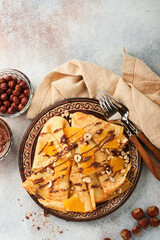 Crepes suzette with oranges and chocolate. Thin crepes with chocolate spread, hazelnuts and orange slices fruit in plate for breakfast on old concrete rustic table background. Copy space. Top view