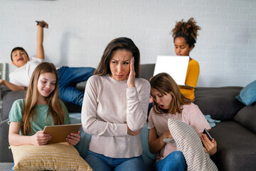 Sad woman with multiethnic children using digital gadgets.. Family and modern technology addiction.