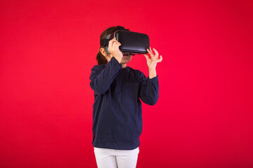 Front view of little girl wearing virtual reality glasses amazed and touching with her hands virtually, on red background. Virtual, augmented reality, technology, games and childhood concept.