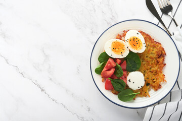 Breakfast. Potatoes latkes with sour cream, spinach salad, tomatoes and boiled eggs on light marble table background.  Delicious food for breakfast. Top view.