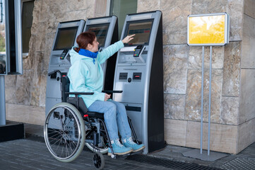 Caucasian woman in a wheelchair buys a train ticket at a self-service checkout. 