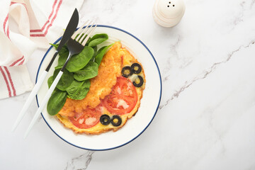 Omelette with tomatoes, black olives, cottage cheese and green spinach herbs on white plate on grey concrete background. Delicious breakfast. Healthy breakfast food. Top view.