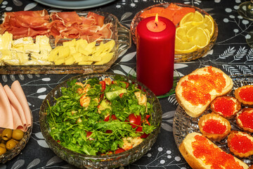 Fragment of the New Year's table with various food and snacks, among which there is a lit candle.