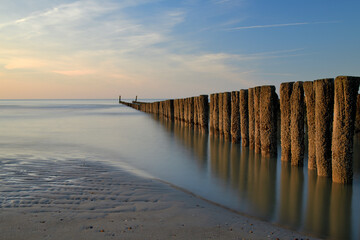 Buhnen stehen am Strand und spiegeln sich im Wasser und das Abendrot
färbt die Wolken leicht rötlich