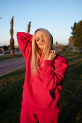 Happy smiling blonde girl in a pink fleece tracksuit has a good time outdoors. The joy of active...