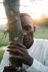 Portrait of a guy peeking out from behind a tree on sunrise 