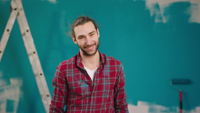 Beautiful charismatic man posing in front of the camera looking straight and smile while end to painting the wall at home. 4k