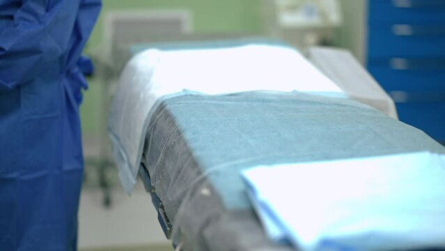 Operation bed in surgery room in hospital with unrecognizable nurse indoors. Surgical bed with sheet prepared for patient in medical clinic. Health care and operations concept