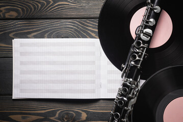 An retro style clarinet, vinyl records and music note book flat lay on the wooden desk background.