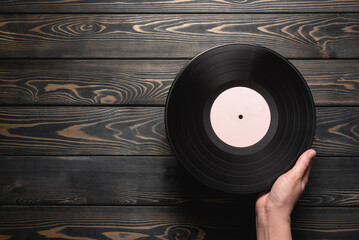 Vinyl record in female hand on wooden flat lay background with copy space.