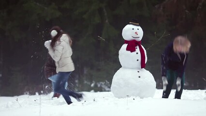 Three girls having snowball fight around a snowman