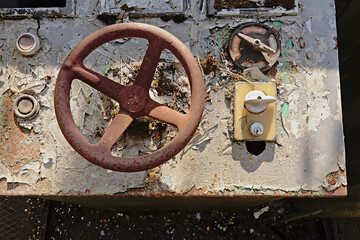  Old decayed control panel with rusty metal steering wheel and bakelite turning knobs and peeling...