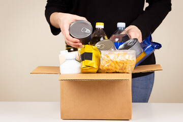 Volunteer woman hands collecting food into donation box. Cardbox full of grocery products....