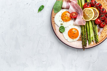 Tasty breakfast. Sunny side up eggs with green asparagus, bacon, ham and and cherry tomatoes. Healthy balanced food. Top view, above, banner