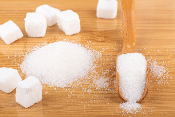 Lump sugar, a pile of sugar and a wooden scoop with white sugar on a wooden background.