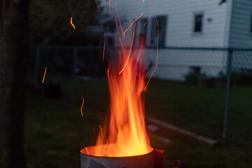 Sparks and flame erupt from the top of a chimney starter on a backyard grill