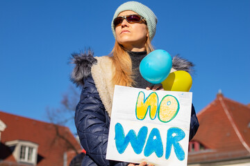A girl at a rally for Ukraine in Germany with a poster of no war and balloons in the color of the...