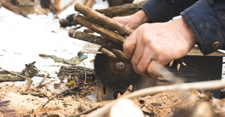 Man cutting wood using stationary circular saw outdoors in winter for kindling close-up view