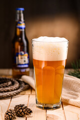 a large glass of beer with foam on wooden boards surrounded by linen and rope - obrazy, fototapety, plakaty