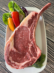 Raw tomahawk steak and peppers